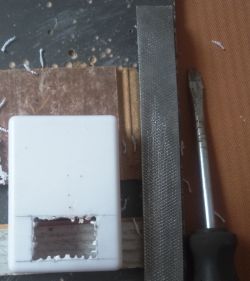 White plastic case with a rectangular cutout, file and screwdriver nearby