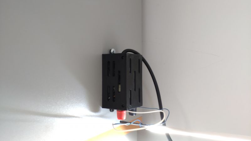 Zbliżenie na moduł elektroniczny z przewodami i obudową zamocowaną na ścianie.