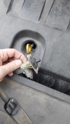 Osoba trzyma część samochodową przed komorą silnika.