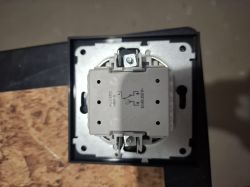 Widok z góry na mechanizm wyłącznika elektrycznego podtynkowego zamontowanego w puszce instalacyjnej.