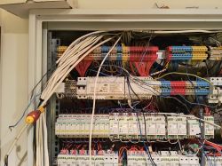 Widok na szafkę elektryczną w nowoczesnym domu z dużą ilością kabli i przewodów.