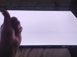 Ręka unosząca panel LCD z widocznymi jaśniejszymi smugami na tle białego podświetlenia