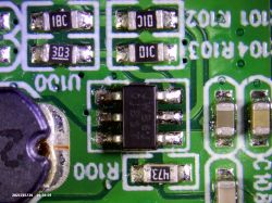 Zbliżenie na układ scalony na zielonej płytce drukowanej z widocznymi elementami elektronicznymi i oznaczeniami.