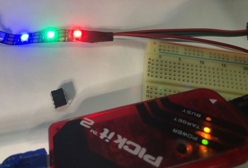 WS2812 LED strip glowing in three colors with Pickit 2 programmer and DIP IC on white surface