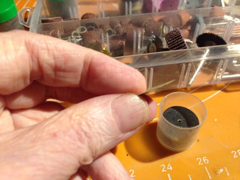 Ręka trzymająca niewielki krążek ścierny, na tle zestawu narzędzi szlifierskich.