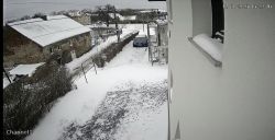 Widok z kamery monitoringu na ośnieżony podjazd z zaparkowanym samochodem.