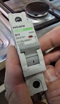 Osoba trzyma wyłącznik nadprądowy Noark B10 na tle płyty grzewczej.