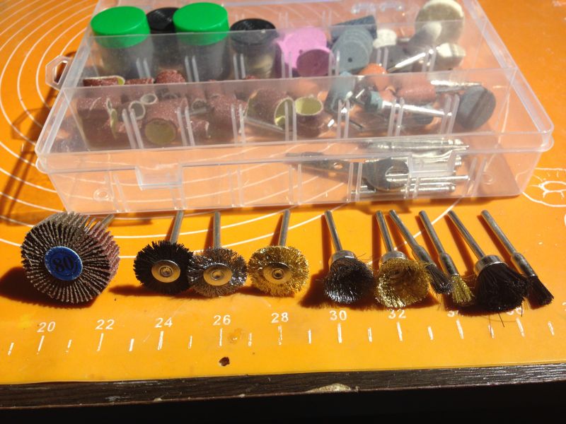 Zestaw akcesoriów do szlifierki z różnymi końcówkami na pomarańczowej macie.