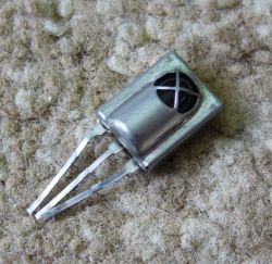 Three-legged metal electronic component lying on a carpet.