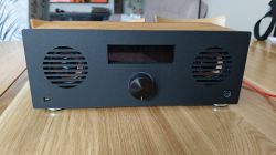 Black rectangular radio with two speakers, a display, and a knob on a wooden table