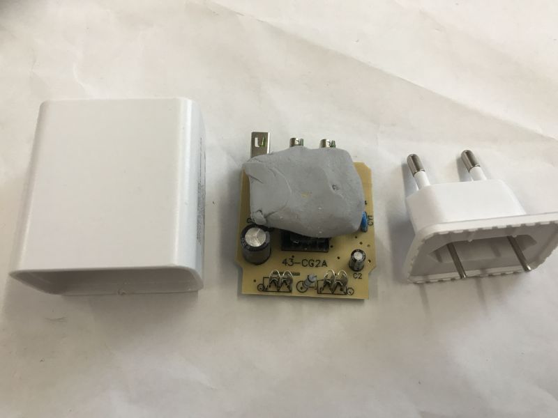 Disassembled plastic USB power adapter with exposed internal PCB and plug