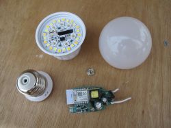 Components of a disassembled LED bulb on a wooden table.