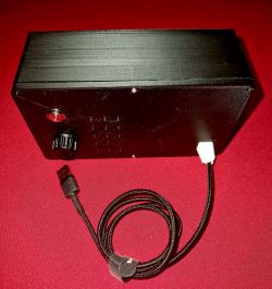 Electronic DIY Project with Cable Black electronic DIY project with a cable on a red background.