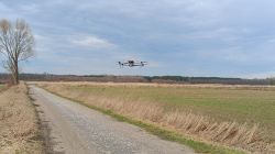 Dron latający nad wiejską drogą otoczoną polami i drzewami.