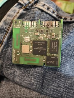 Uszkodzony moduł elektroniczny PCB z przypalonymi stykami, leżący na dżinsach