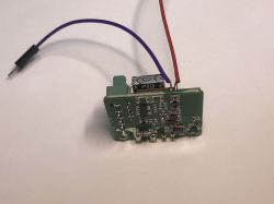 ATLO-SW1-TUYA Relay Module During Programming ATLO-SW1-TUYA relay module PCB with red and purple power/programming wires soldered on.