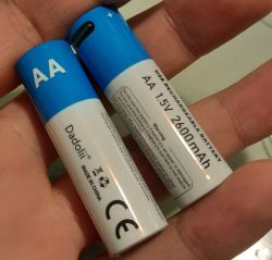 Two AA batteries in a hand, one with visible markings Dadolii and specification 1.5V 2600mAh.
