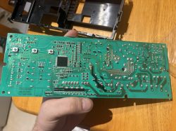 Zielona płytka PCB z układami SMD i punktami lutowniczymi, trzymana w dłoni na drewnianym stole