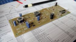 Zbliżenie na płytkę drukowaną z zamontowanymi komponentami elektronicznymi leżącą na dokumentacji technicznej.