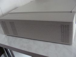 Szara obudowa komputera typu desktop z poziomymi żaluzjami, na blacie przy ścianie