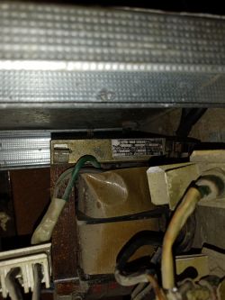Widok transformatora elektrycznego z widocznymi kablami i złączami w środowisku przemysłowym.