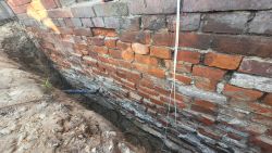 Odkopana ceglana ściana fundamentowa budynku z widoczną rurą drenarską