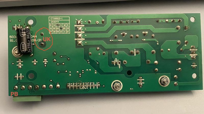 Spód zielonej płytki PCB z kondensatorem 220 µF 50 V; czerwone oznaczenia „UK” i „PB”.