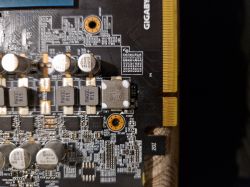 Zdjęcie fragmentu PCB karty graficznej GTX 1660 Ti Gigabyte z widocznymi kondensatorami, cewkami indukcyjnymi i oznaczeniem białymi kropeczkami.