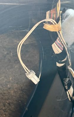 Zdjęcie przedstawia luźny przewód elektryczny z białą wtyczką w bagażniku samochodu.