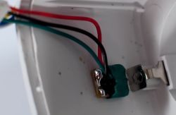 Close-up inside a housing with red, black, and green wires connected to a metal clamp in green compound.