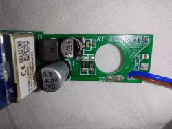 Energy meter PCB with round current-transformer opening Close-up of a green PCB with a round CT hole, capacitors, and a brown and blue wire soldered to it