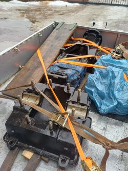 Duży czarny element metalowy przypięty pasami transportowymi na platformie przyczepy