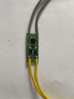 Zielona płytka drukowana z elementami elektronicznymi oraz czterema przewodami: dwoma szarymi i dwoma żółtymi.