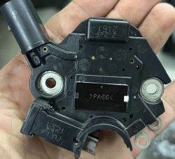 Widok ręki trzymającej regulator napięcia alternatora z oznaczeniami modelu.