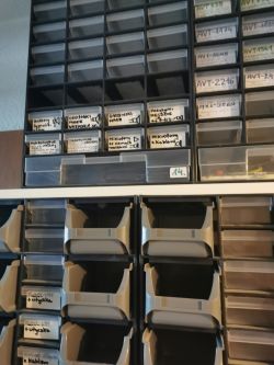 Plastikowe organizery z szufladkami na części elektroniczne, oznaczone ręcznie etykietami.