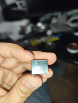 Ręka trzymająca przekaźnik z oznaczeniami elektrycznymi.
