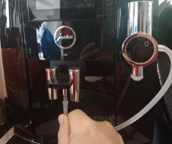 Ekspres do kawy Jura S8 zbliżenie na wylewkę i podłączaną rurkę systemu mlecznego, trzymaną przez dłoń.