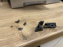 Złamany plastikowy element z metalową sprężyną, leżący na drewnianym blacie