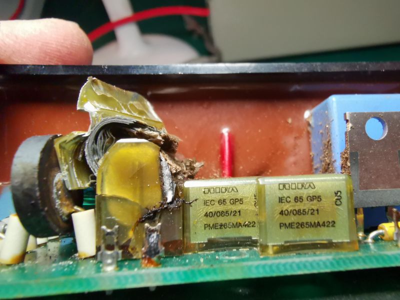 Damaged RIFA paper capacitor on a PCB, partially blown open with foil exposed