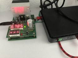 Green circuit board with red LED readout 6.785 next to a black UPS unit and cables