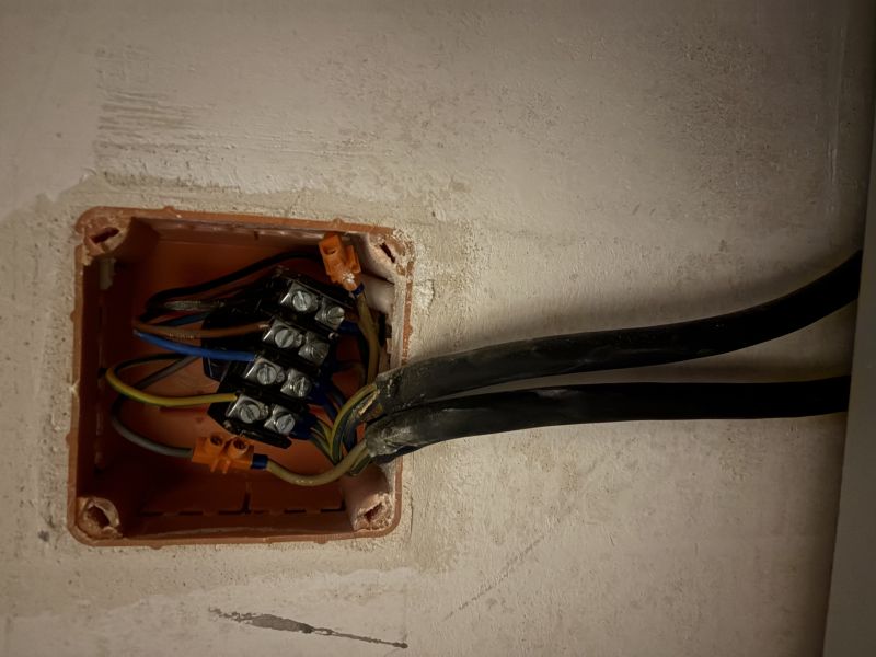 Otwarta puszka elektryczna w ścianie z listwą zaciskową i kilkoma przewodami z czarną izolacją
