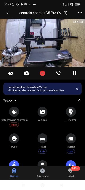 Drukarka 3D na stole w drewnianym pomieszczeniu monitorowana przez aplikację