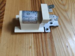 Filtr przeciwzakłóceniowy z oznaczeniami elektrycznymi na boku, leżący na drewnianym blacie