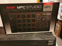 Pudełko kontrolera muzycznego AKAI Professional MPC Studio stojące na czarnym futerale, w tle sprzęt elektroniczny.