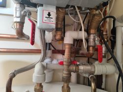 Instalacja hydrauliczna z plastikowymi i metalowymi rurami, zawory z czerwonymi uchwytami.