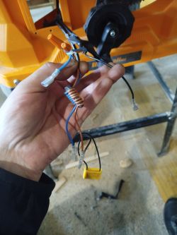 Ręka trzymająca kilka przewodów elektrycznych z końcówkami i złączkami przy żółtym urządzeniu.