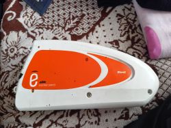 Biała i pomarańczowa bateria roweru elektrycznego BionX Electric Series leży na wzorzystym kocu.