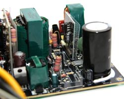 Zbliżenie płytki PCB z elementami zasilacza: kondensator, transformatory i radiator