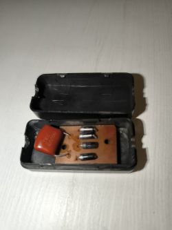 Zbliżenie na otwarty plastikowy mostek prostowniczy z widocznymi diodami i kondensatorem.