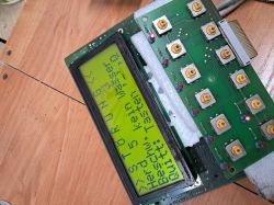 Zbliżenie na uszkodzony wyświetlacz LCD przymocowany do płytki drukowanej z przyciskami.
